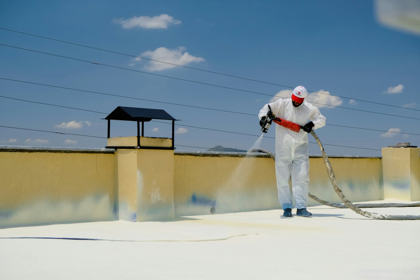 Technician sprays white insulation onto a flat rooftop.