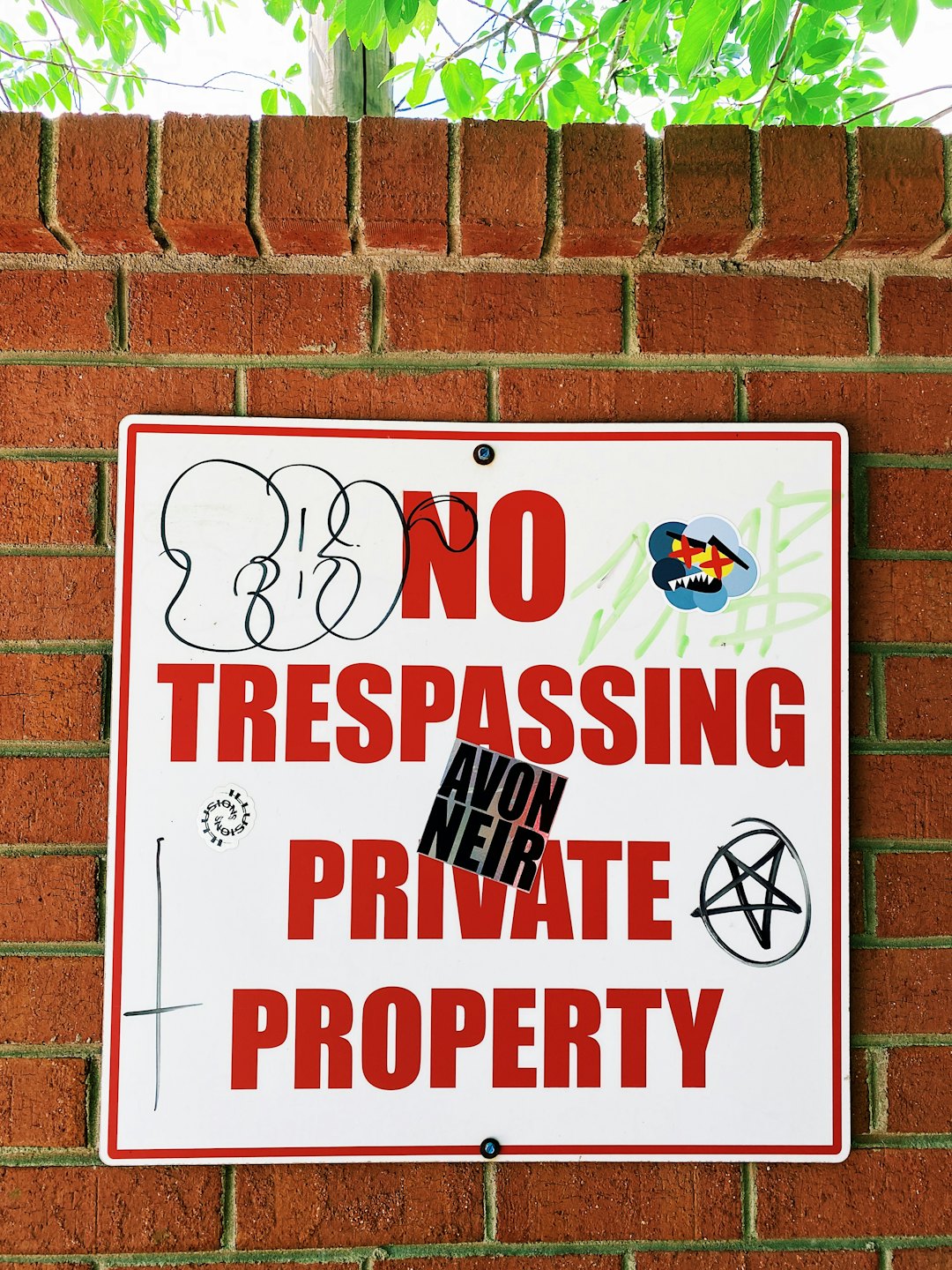 Graffiti covered no trespassing sign attached to a brick wall.