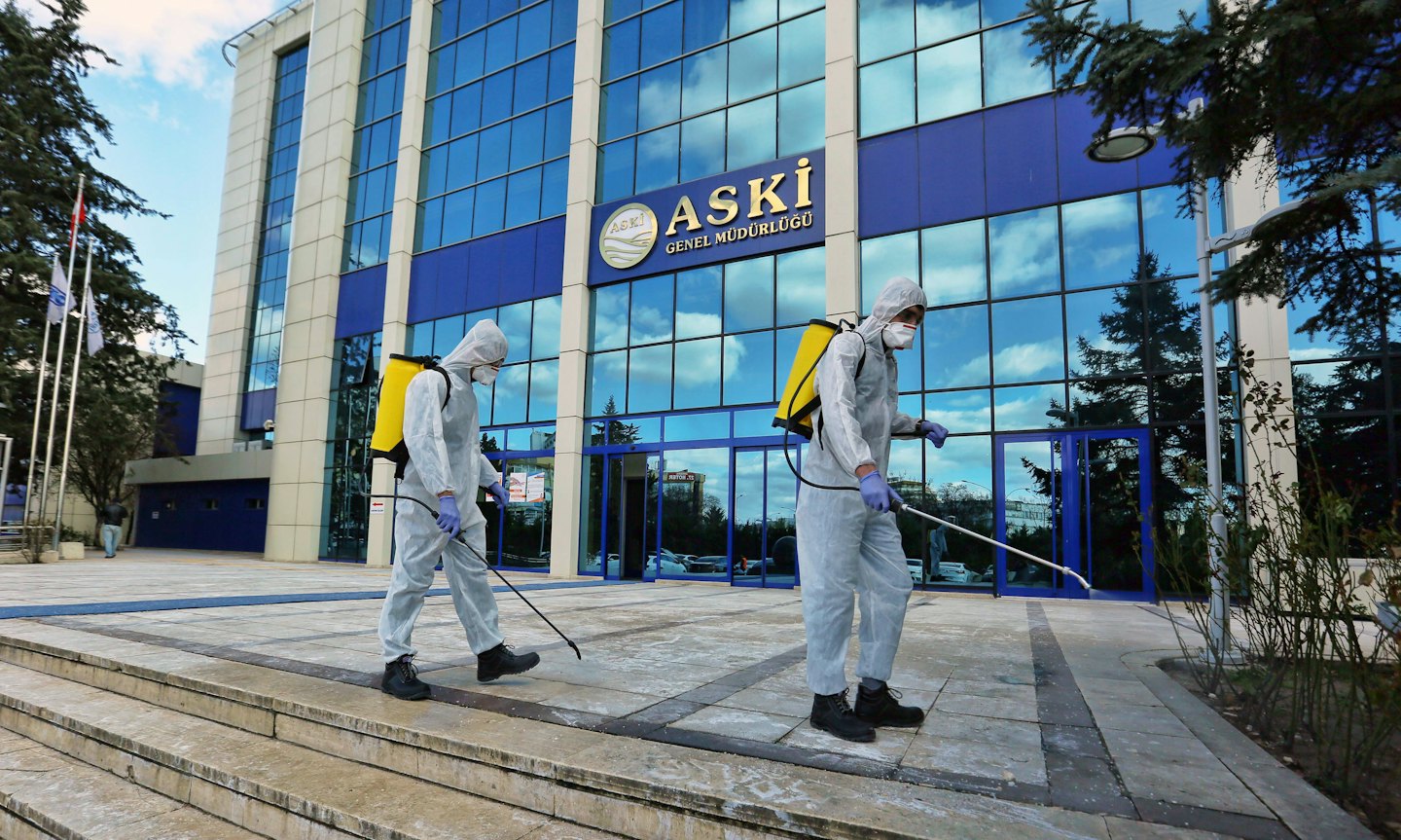Two people in hazmat suits disinfect office building steps.